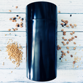 Large black seed storage vault container with vacuum-seal top on white wooden surface with scattered seeds