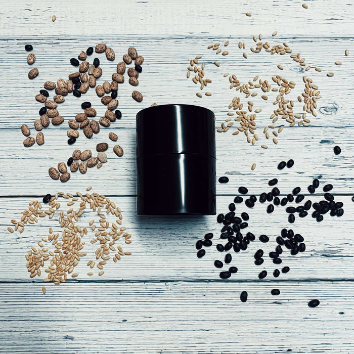 Extra-small black Seed Storage Vault surrounded by various seeds on a wooden surface